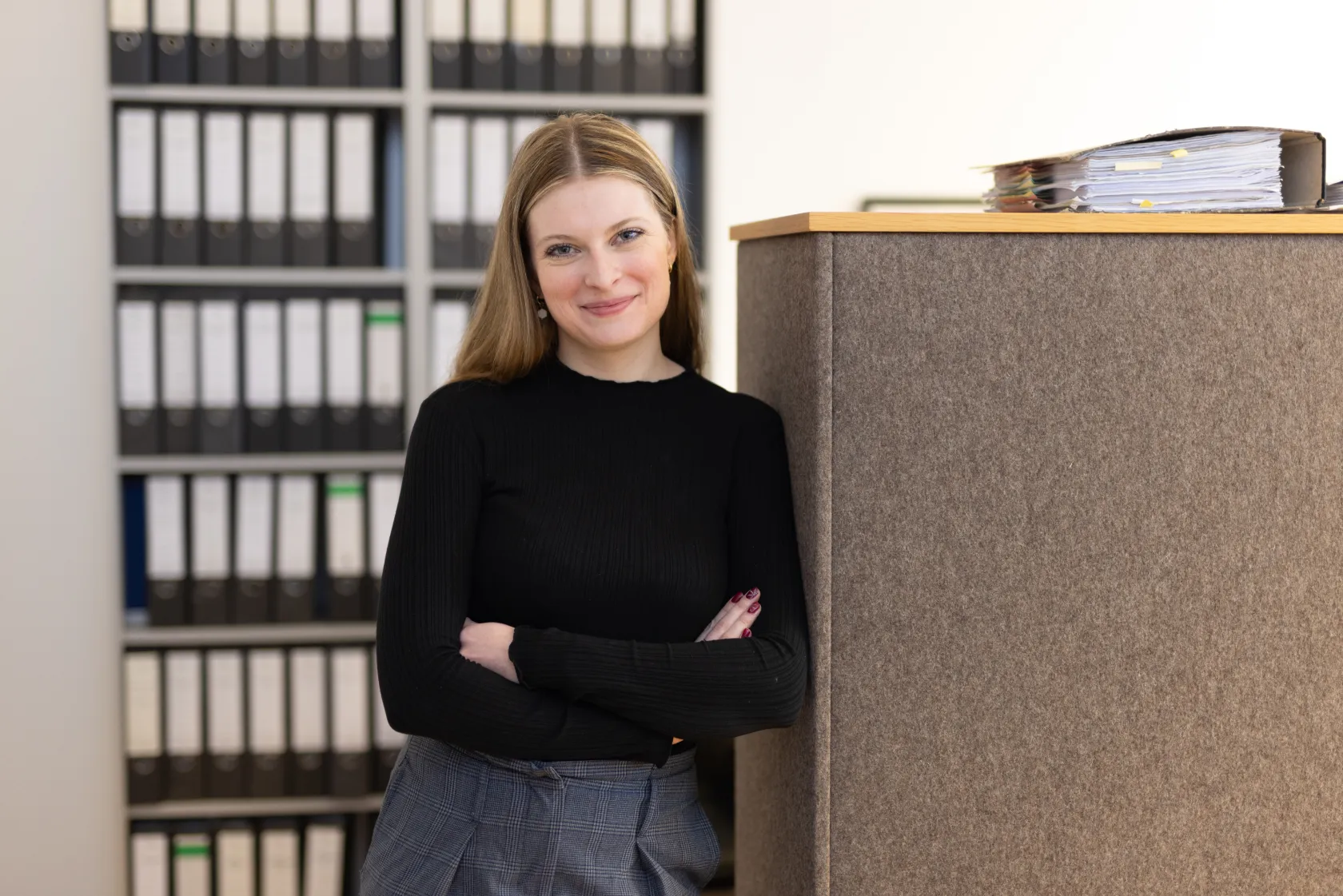 Mitarbeiterin steht im Büro und lächelt in die Kamera